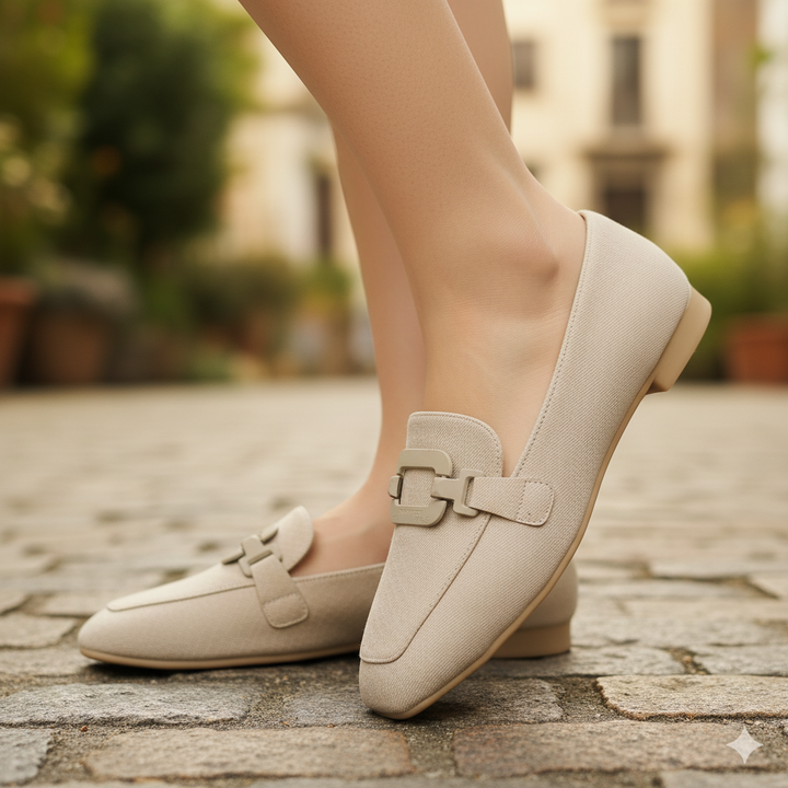 Beige loafers worn on a stone pavement with a blurred background
