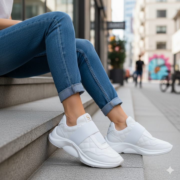Person wearing white sneakers and blue jeans sitting on steps in an urban setting