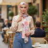 Woman wearing a floral hijab and beige blouse in an outdoor cafe setting